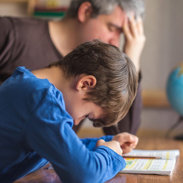 Un petit garçon fait tristement ses devoirs avec son père
