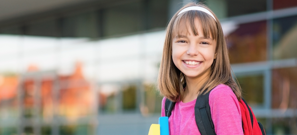 Une écolière souriante devant son école